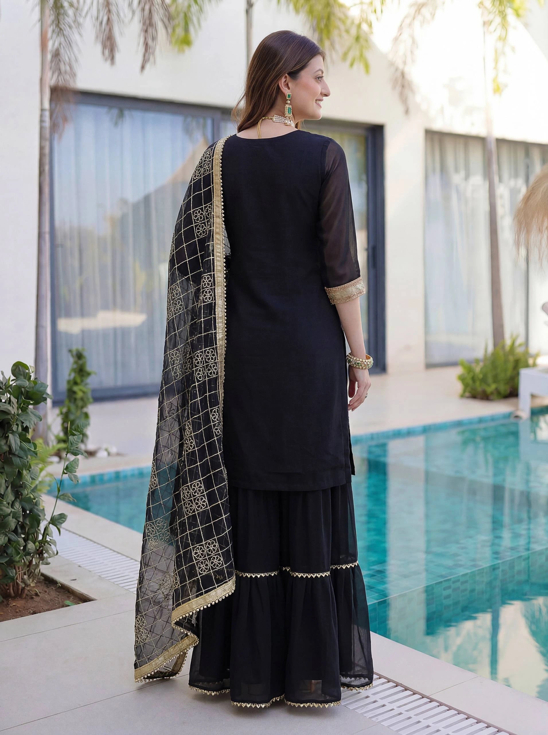 Woman in a black traditional outfit with a patterned dupatta by a poolside.